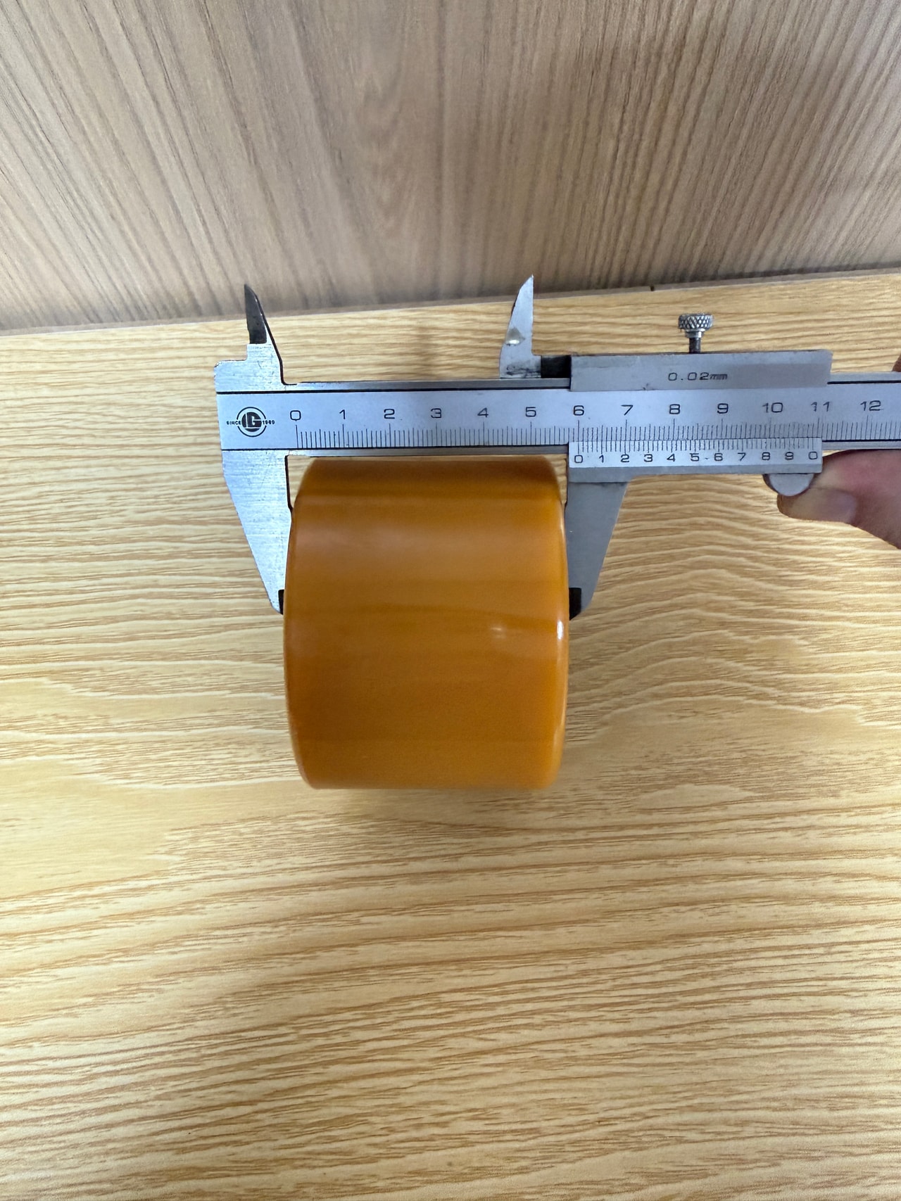 Vernier caliper measuring the face width of an amber polyurethane roller, with ruler markings visible